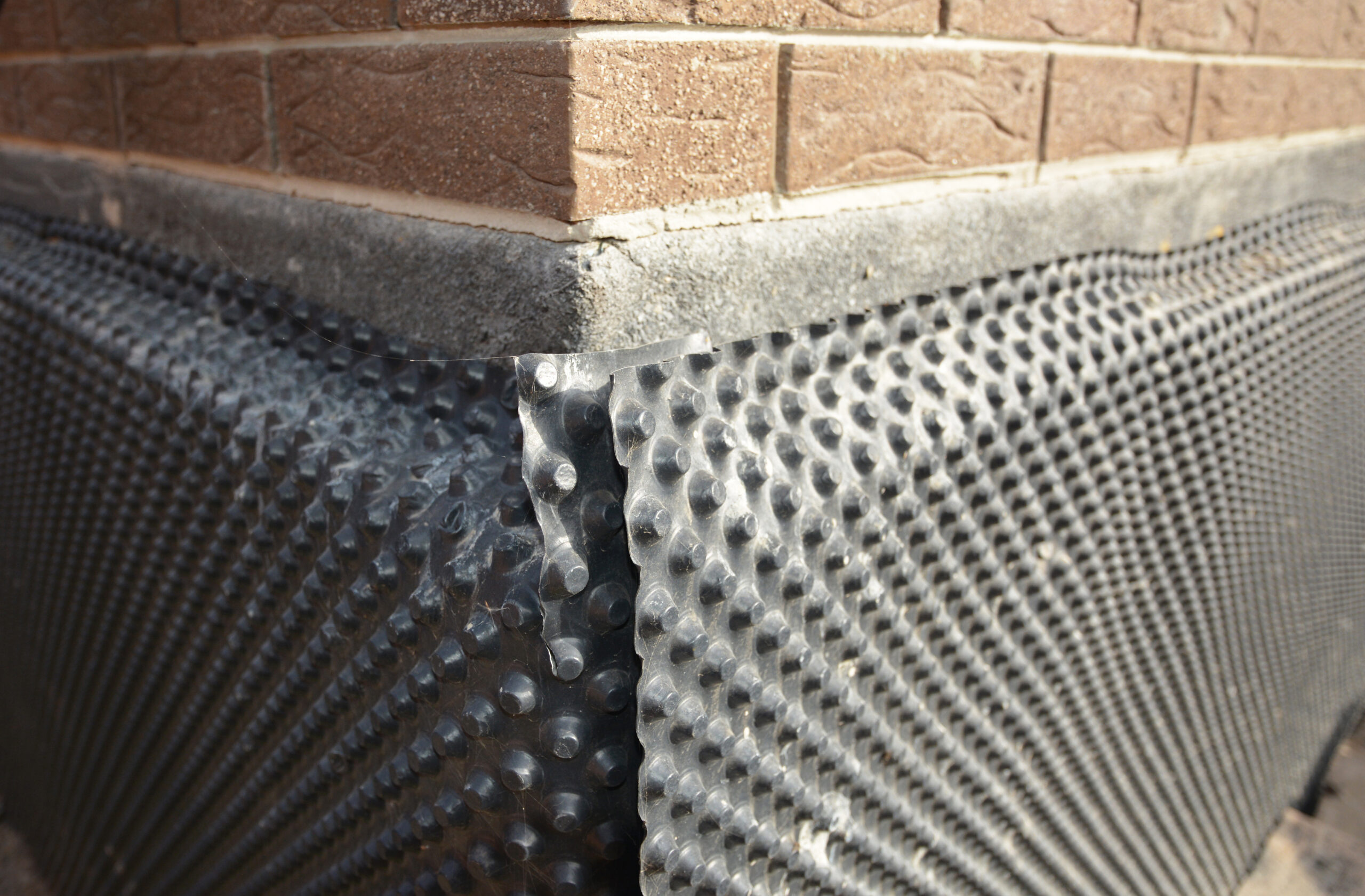 Basement waterproofing outdoors. Installation of a dimpled waterproofing membrane on the exterior basement foundation wall.